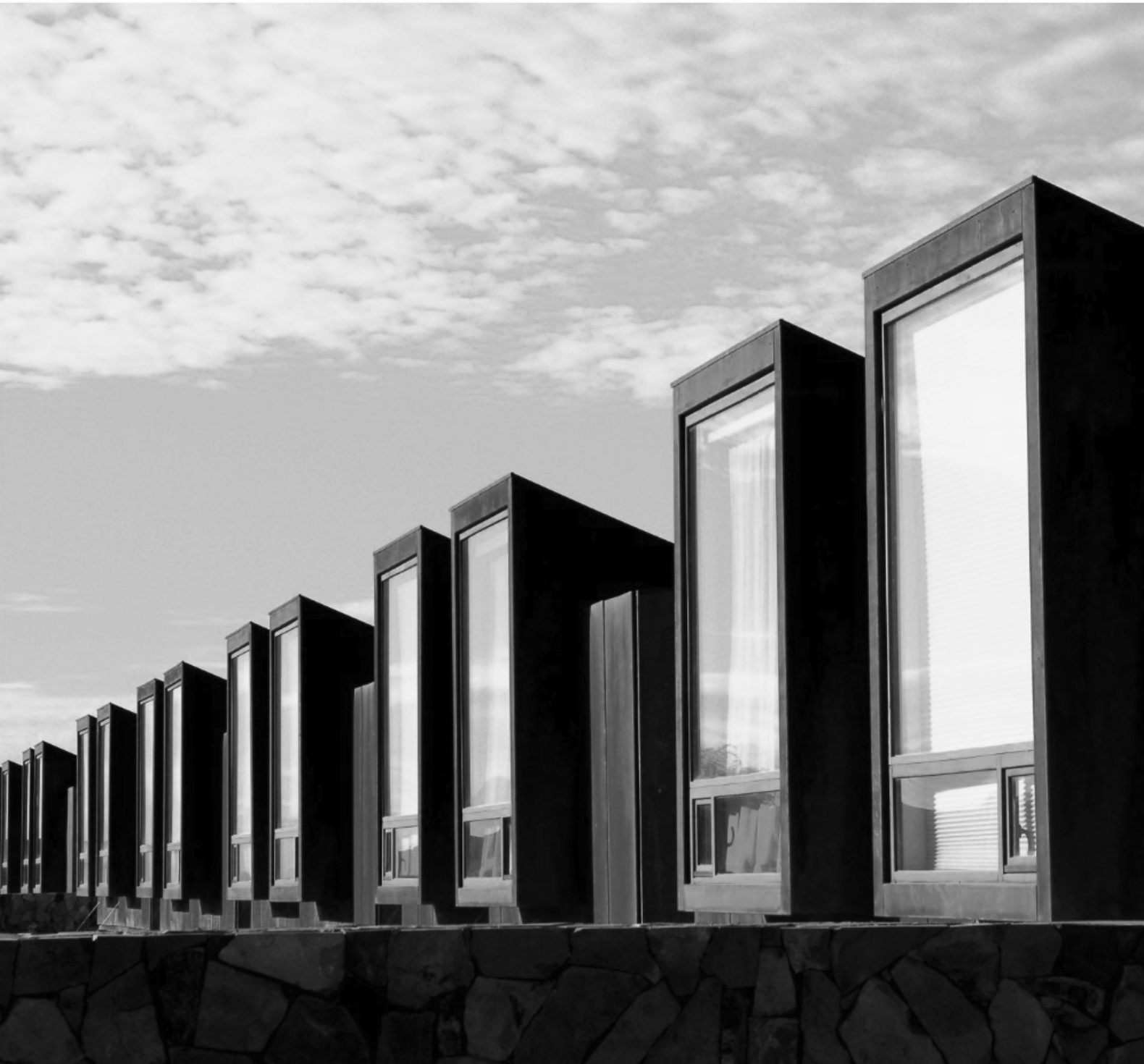 Serie de volúmenes oscuros con ventanales sobre un muro de piedra